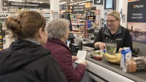 A resident shops with a home helper at a Turku grocery checkout, using a list to manage an assisted everyday errand.